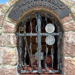 Kovaný památník svatých s atributy na mřížích. Sv. Brigita Švédská - hůl, Sv. Benedikt - medailon