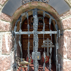Schmiedeeisernes Denkmal der Heiligen mit Attributen auf dem Gitter. Feuergefäß und das libanesische Kreuz