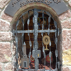 Kovaný památník s atributy svatých. Sv. Tomáš Akvinský - kostel, Sv. Norbert - monstrance