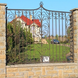 Grille de clture en fer forg encastre dans le mur en pierre. Cre de barreaux carrs et volutes.  